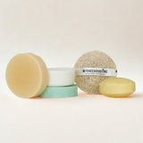 Set of natural skincare products including a bar of soap, a scrub, and a bath bomb on a white background.