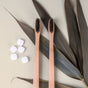 Two bamboo toothbrushes on a beige surface with dried leaves and white tablets.