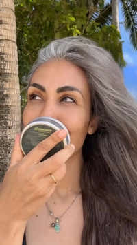 Woman with gray hair holding a container outdoors with trees and sky in the background
