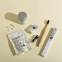 Collection of dental care products including toothpaste tablets, a toothbrush, and packaging on a beige background.