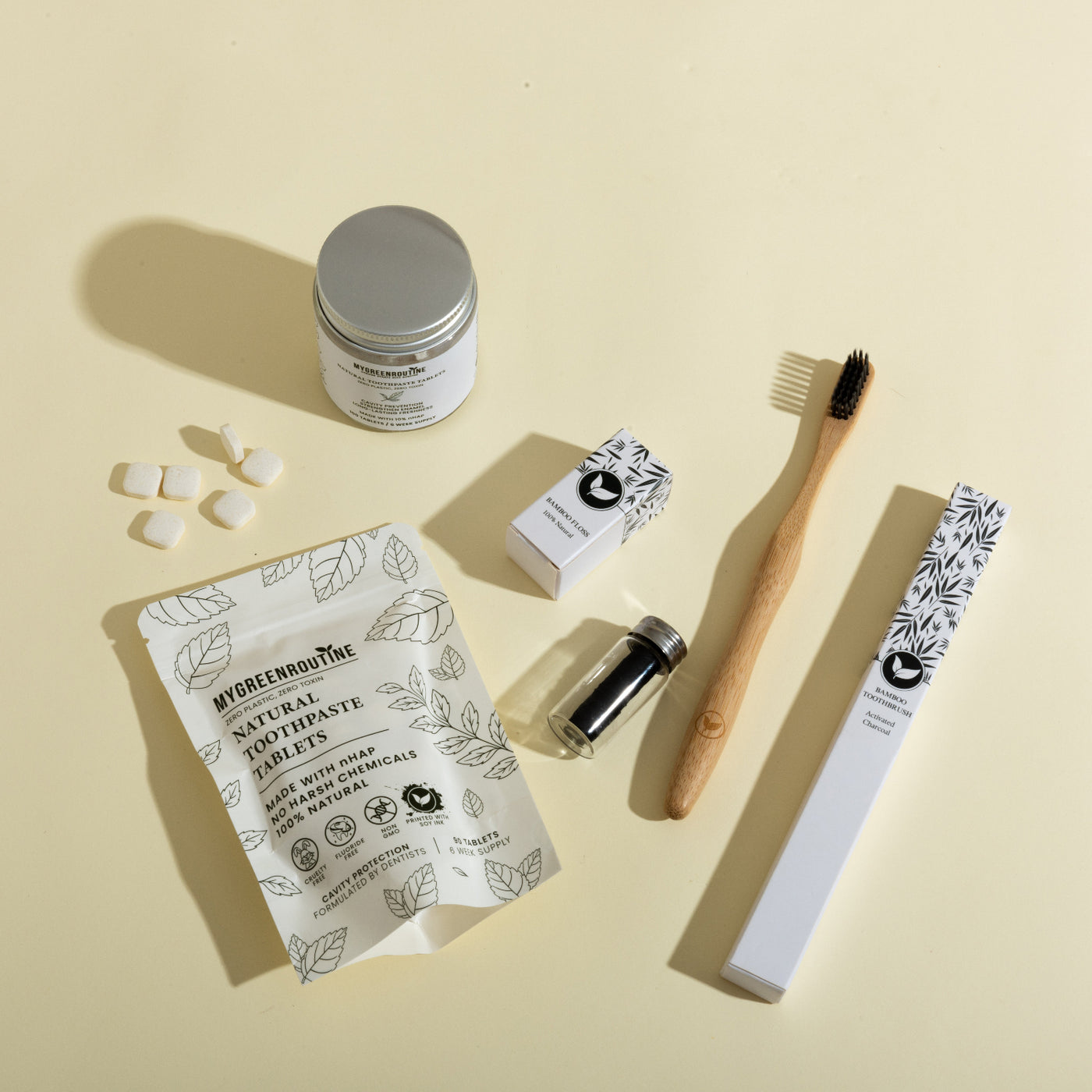 Collection of dental care products including toothpaste tablets, a toothbrush, and packaging on a beige background.