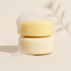 Two stacked shampoo bars with bubbles on a light beige background