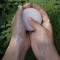 Hands holding a white ball against a green leafy background