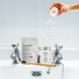 Hand pouring tablets from a container into a sink with dental care products on a white background