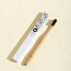 Bamboo toothbrush with black bristles and a leaf patterned handle on a beige background