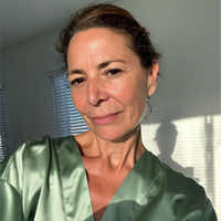 Woman wearing a green satin robe in a room with sunlight filtering through blinds.